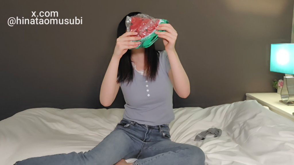 ベッドに座った黒髪の女性が、透明包装に入ったスイカ柄インフレータブルボール(赤い果肉部分が見える)を両手で顔の前に掲げている様子