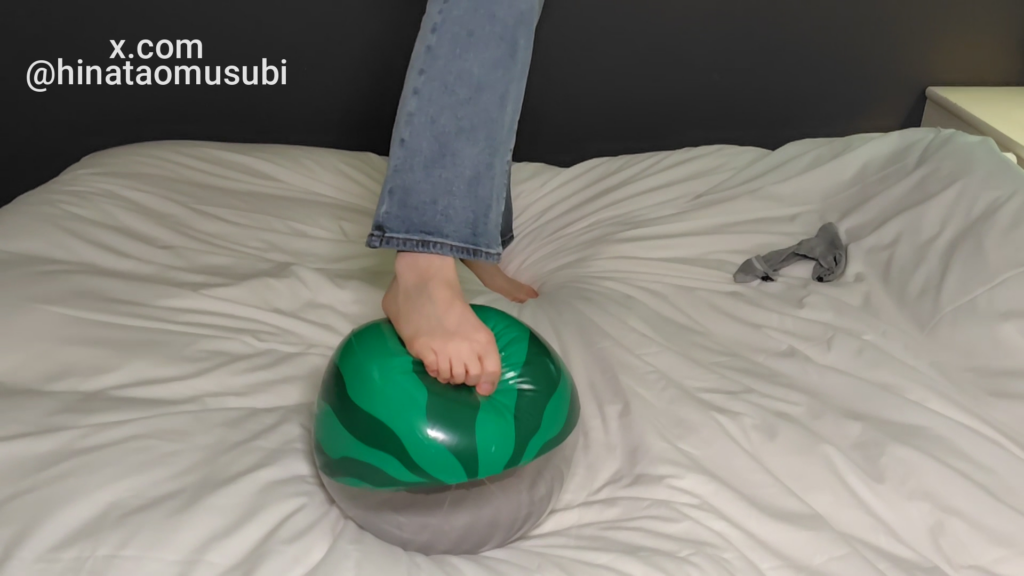 ベッドの上で素足で緑色のスイカ柄ビーチボールを優しく踏んでいる脚のクローズアップ