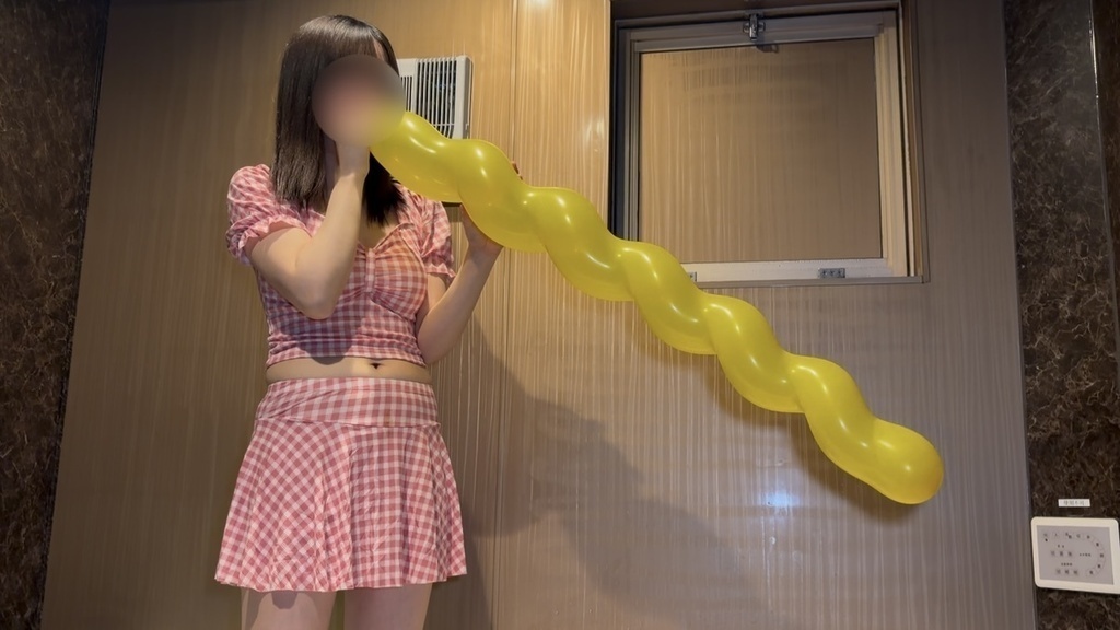 おへそが見える水着の女の子が風船を口で膨らましている